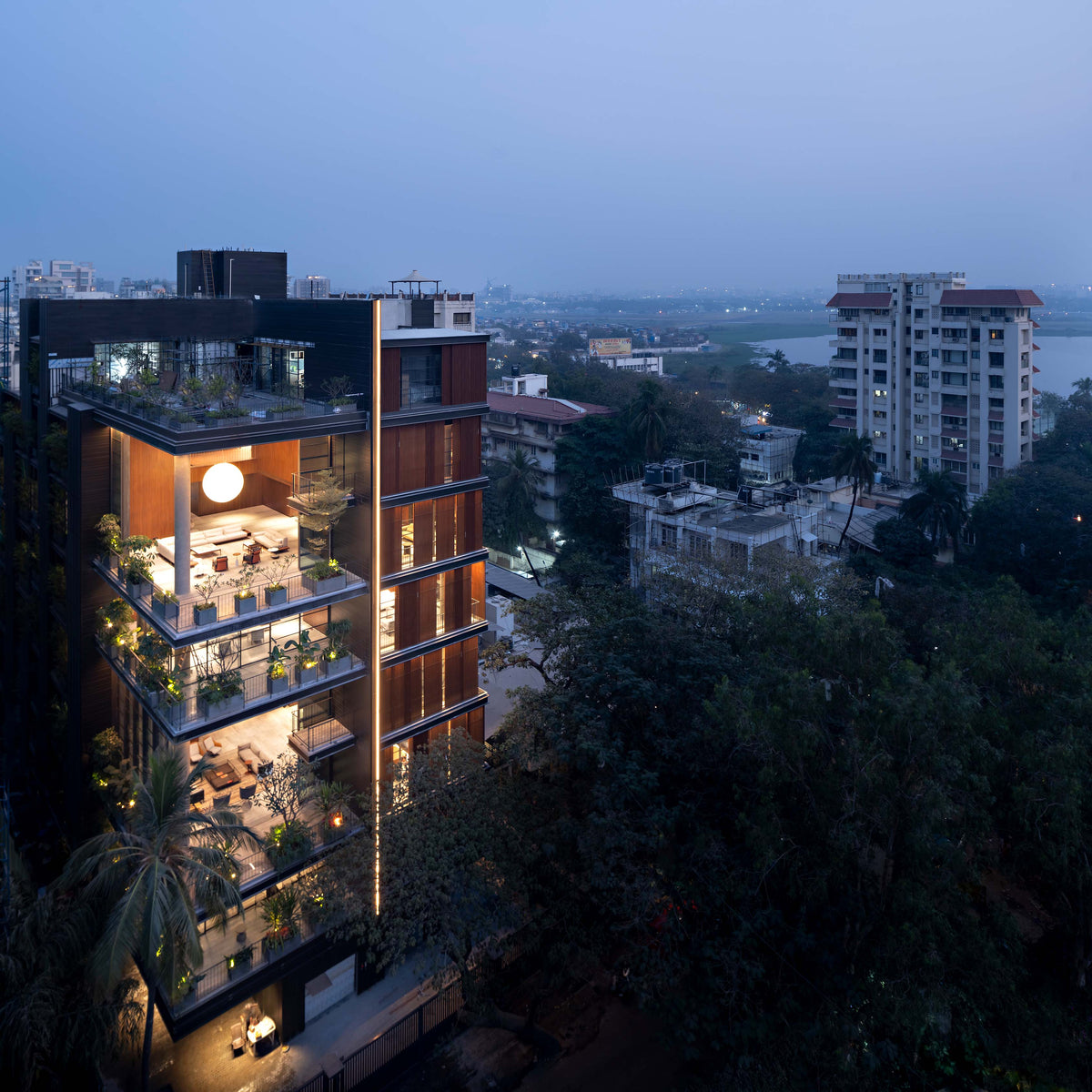 Shiv Kunj lit at dusk above the Juhu treetops, creek and low rooftops behind
