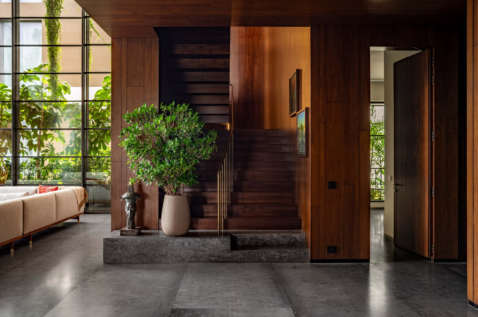 Entrance hall in teak panelling with a stair on a stone plinth and a potted tree