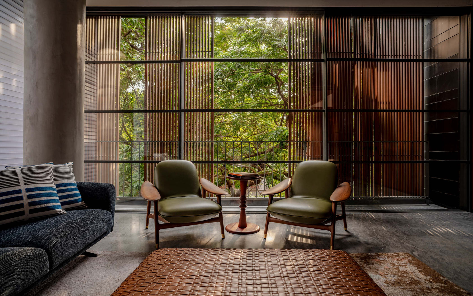 Two green leather armchairs at a floor-to-ceiling timber screen, a tree filling the window