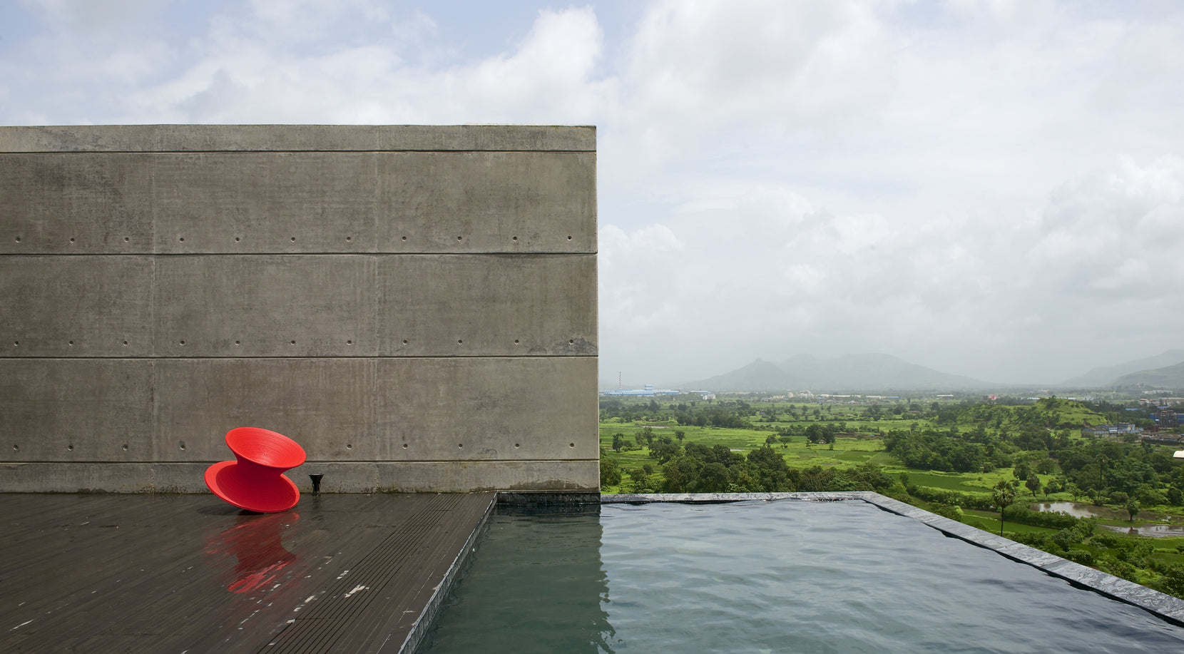 Red moulded chair against a concrete wall at the pool edge, green valley and hills behind