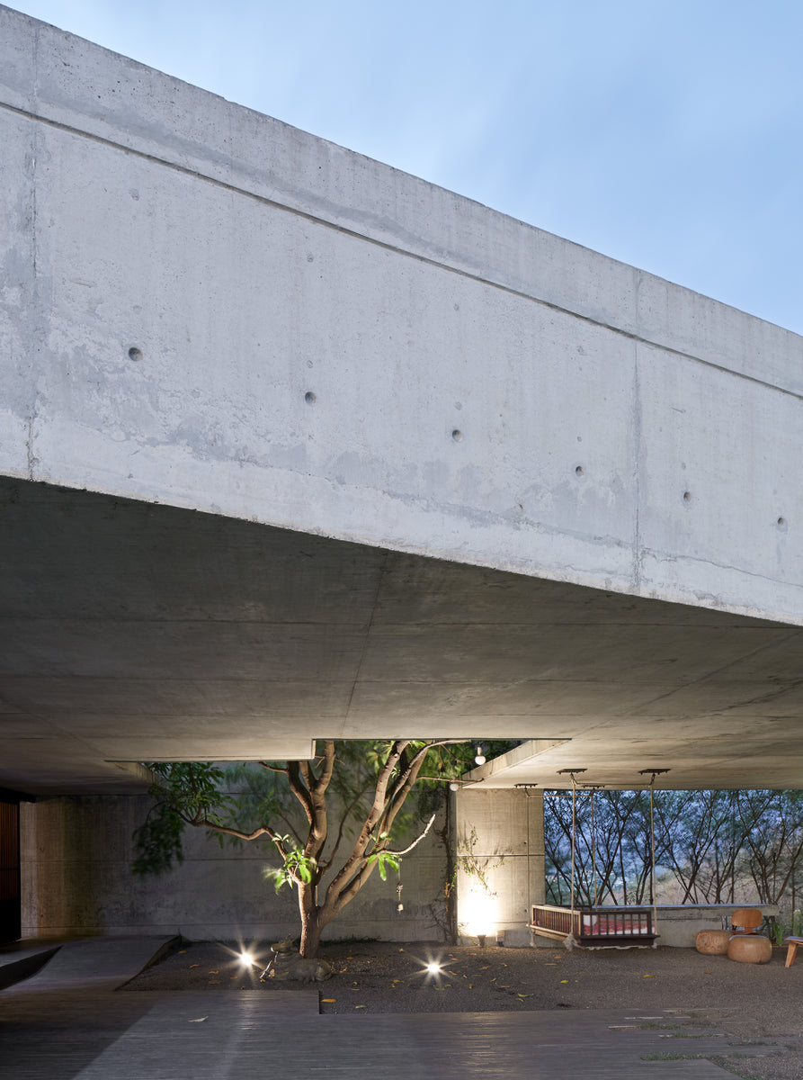 Deep concrete cantilever overhanging the entrance court, a lit tree growing beneath