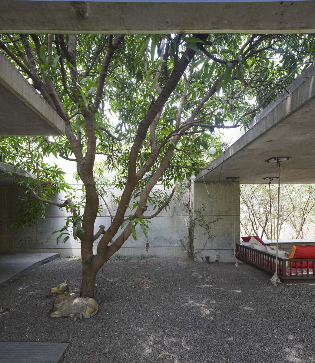 Gravel courtyard with a hanging daybed in red under the tree and low concrete soffits