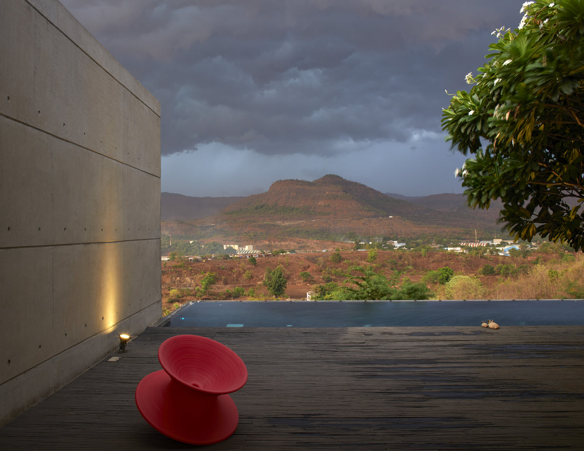 The House Cast in Liquid Stone: a red disc chair on the deck above the pool, hills beyond