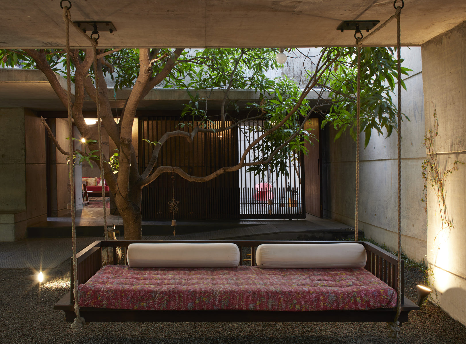 Rope-hung daybed with a kantha cover framed by the courtyard tree and a timber screen