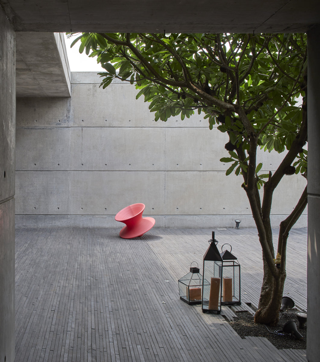 Pink chair and glass lanterns on the stone terrace, frangipani shading the concrete wall