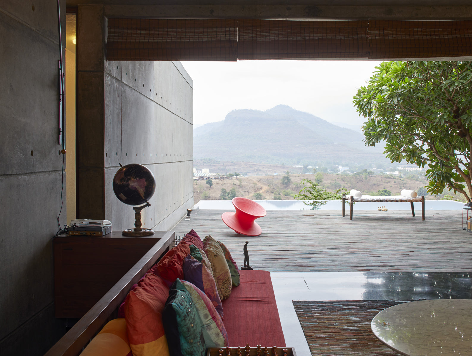 Living room cushions and a globe framing the open terrace, red chair and hills beyond