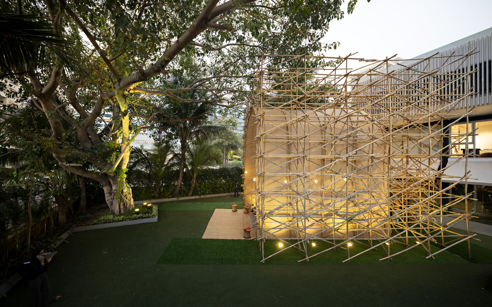 Installation from above the lawn, its fabric drum ringed by bamboo and uplit at dusk